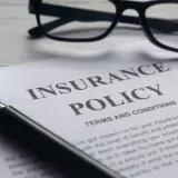 Okulary, lupa i dokument "Insurance Policy" symbolizują analizę polisy PZU po śmierci teścia.