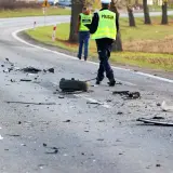 Na drodze po wypadku leżą szczątki pojazdów i opona. Policjanci w kamizelkach odblaskowych badają miejsce zdarzenia, być może szukając śladów ucieczki z miejsca wypadku.