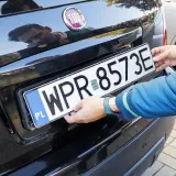 Ręce montują tablicę rejestracyjną. Uniknięcie mandatu za brak tablicy rejestracyjnej jest ważne.