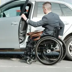 Mężczyzna na wózku inwalidzkim wsiada do samochodu. Ubezpieczenie samochodu a stopień niepełnosprawności to ważna kwestia dla osób z niepełnosprawnościami.