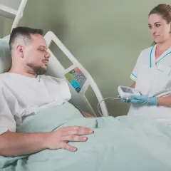 Uśmiechnięta pielęgniarka z aparatem do pomiaru ciśnienia w rękach, pacjent w łóżku szpitalnym. Radość z zakończenia leczenia.