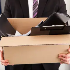 Mężczyzna w garniturze niesie karton z rzeczami. Ubezpieczenie od utraty pracy daje poczucie bezpieczeństwa w trudnych chwilach.