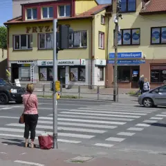 Kobieta czeka na zielone światło na pasach, kiedy należy zachować szczególną ostrożność. Samochody zbliżają się do przejścia.