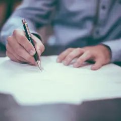 Dłoń pisze długopisem na dokumencie. Zastanawiasz się, kiedy wypowiedzieć OC? Czas na decyzję!
