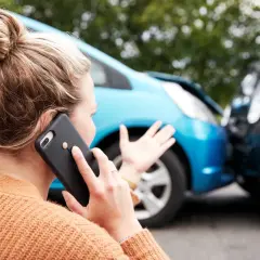 Kobieta po wypadku samochodowym dzwoni po pomoc, martwiąc się o wartość ubezpieczeniową swojego pojazdu.