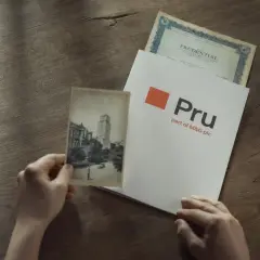 Ręce trzymają stare zdjęcie i dokument z logo Pru, part of M&G plc. To pokazuje, że Prudential to firma z długą historią.