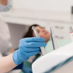 Ręka w niebieskiej rękawiczce trzyma wiertło stomatologiczne. Pacjent leży na fotelu. Może to być początek skargi na prywatnego stomatologa.