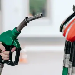 Dłoń trzyma zielony pistolet dystrybutora paliwa. Czy to benzyna 95 czy 98? Różnica jest ważna dla silnika.