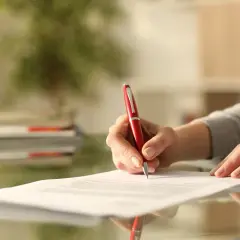 Dłoń pisze czerwonym długopisem na dokumencie. Zastanawiam się, co dalej, gdy nie wypowiedziałem umowy OC.