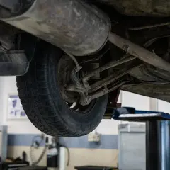Podnośnik samochodowy ukazuje podwozie auta, gdzie widać koło i elementy zawieszenia. Może to być etap przygotowań do zwrotu autocasco po sprzedaży samochodu.