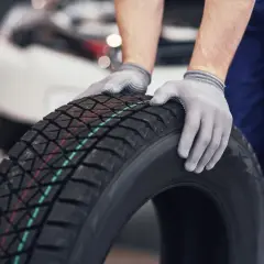Mechanik w rękawiczkach trzyma oponę zimową. Czy w Polsce jest obowiązek zmiany opon na zimowe? Odpowiedź brzmi: nie.