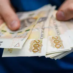 Dłonie trzymające plik banknotów 200 zł. Może to być związane z zajęciem komorniczym, gdy pieniądze są przekazywane.