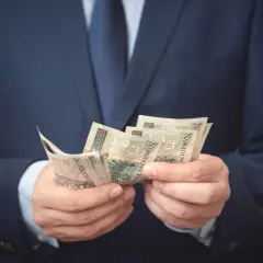 Mężczyzna w garniturze liczy banknoty. Może to symbolizować otrzymanie odszkodowania i zadośćuczynienia po trudnym zdarzeniu.