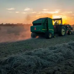 Traktor z prasą zbiera siano o zachodzie słońca. Dbałość o ubezpieczenie rolnicze zapewnia spokój ducha.