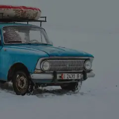Niebieski, stary samochód z bagażem na dachu stoi na śniegu. Widać, że to auto z czasów PRL-u, do jakiego wieku auta jeździli Polacy.