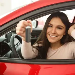 Uśmiechnięta młoda kobieta trzyma kluczyki do czerwonego auta. Szuka sposobów na tanie OC, by cieszyć się jazdą bez nadwyrężania budżetu.