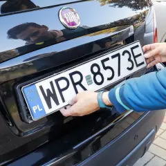 Ręce montują tablicę rejestracyjną. Uniknięcie mandatu za brak tablicy rejestracyjnej jest ważne.