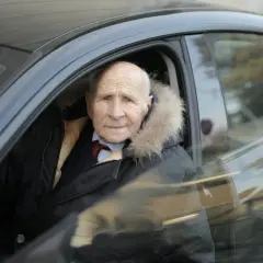 Starszy pan w zimowej kurtce z futrzanym kołnierzem siedzi za kierownicą. Szuka zniżki OC dla emerytów.