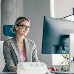 Kobieta w okularach pracuje przy komputerze, analizując oferty ubezpieczeń nieobowiązkowych.