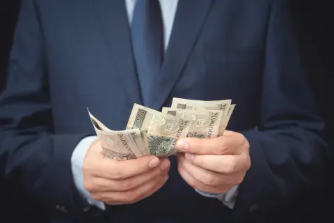 Mężczyzna w garniturze liczy banknoty. Może to symbolizować otrzymanie odszkodowania i zadośćuczynienia po trudnym zdarzeniu.