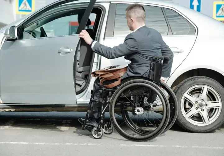 Mężczyzna na wózku inwalidzkim wsiada do samochodu. Ubezpieczenie samochodu a stopień niepełnosprawności to ważna kwestia dla osób z niepełnosprawnościami.