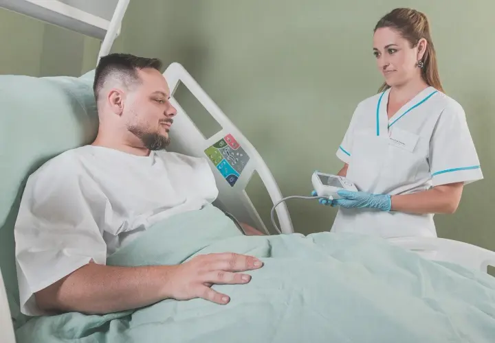Uśmiechnięta pielęgniarka z aparatem do pomiaru ciśnienia w rękach, pacjent w łóżku szpitalnym. Radość z zakończenia leczenia.