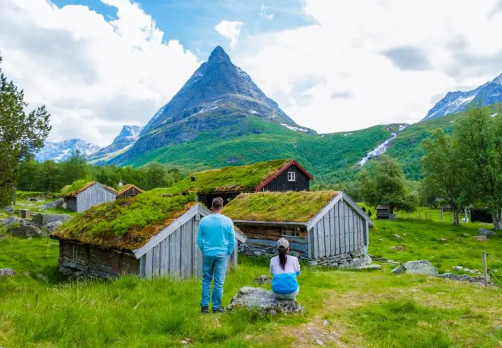 Para planujących ubezpieczenie Norwegia: para podziwia malownicze chatki z zielonymi dachami i górski krajobraz.