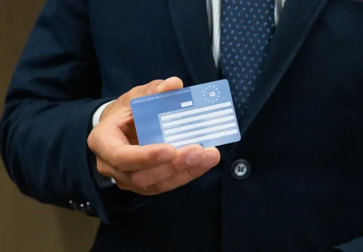 Mężczyzna trzyma Europejską Kartę Ubezpieczenia Zdrowotnego. Ważność karty EKUZ jest kluczowa dla podróżujących po Europie.