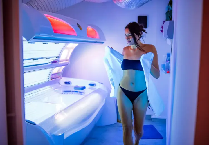 Kobieta w bikini wychodzi z solarium, niosąc ręcznik. Uważaj na oparzenie po solarium, bo może być bolesne.