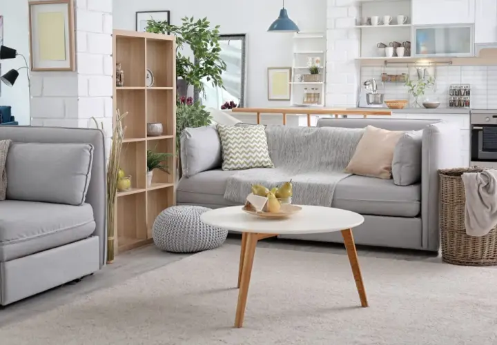 Nowoczesny salon z aneksem kuchennym. Miękka sofa, stolik kawowy z owocami i kosz na pranie. To wszystko warto objąć ubezpieczeniem mienia.