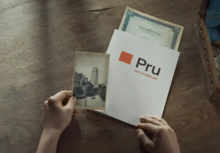 Ręce trzymają stare zdjęcie i dokument z logo Pru, part of M&G plc. To pokazuje, że Prudential to firma z długą historią.