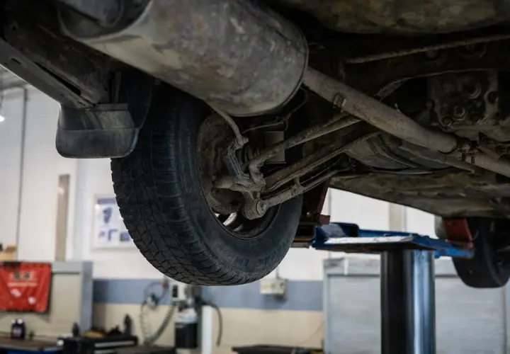 Podnośnik samochodowy ukazuje podwozie auta, gdzie widać koło i elementy zawieszenia. Może to być etap przygotowań do zwrotu autocasco po sprzedaży samochodu.