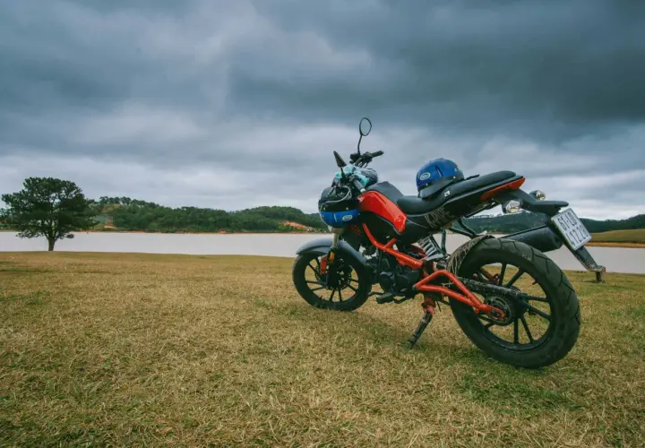 Czerwono-czarny motocykl z niebieskim kaskiem na siedzeniu, gotowy do jazdy nad jeziorem.
