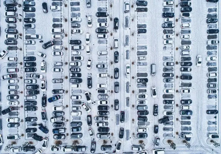 Zimowy parking z wieloma samochodami. Wygląda, jakby druga rata OC po terminie, bo tyle aut stoi w śniegu.