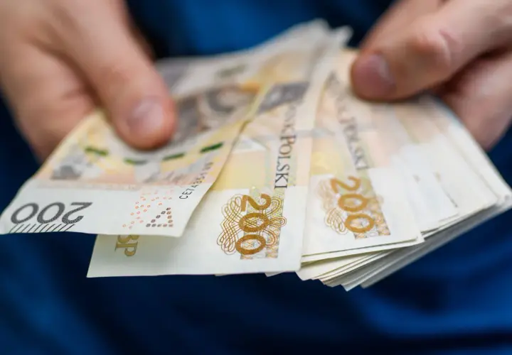 Dłonie trzymające plik banknotów 200 zł. Może to być związane z zajęciem komorniczym, gdy pieniądze są przekazywane.