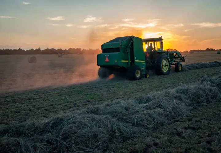 Traktor z prasą zbiera siano o zachodzie słońca. Dbałość o ubezpieczenie rolnicze zapewnia spokój ducha.