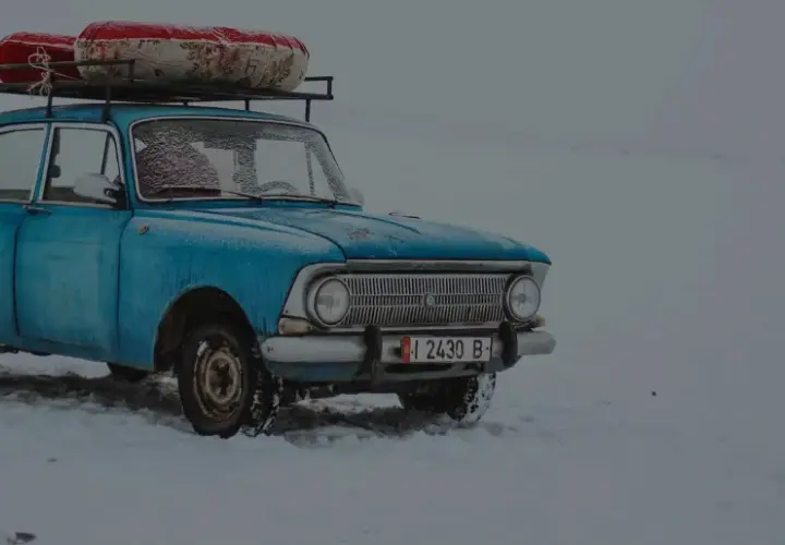 Niebieski, stary samochód z bagażem na dachu stoi na śniegu. Widać, że to auto z czasów PRL-u, do jakiego wieku auta jeździli Polacy.