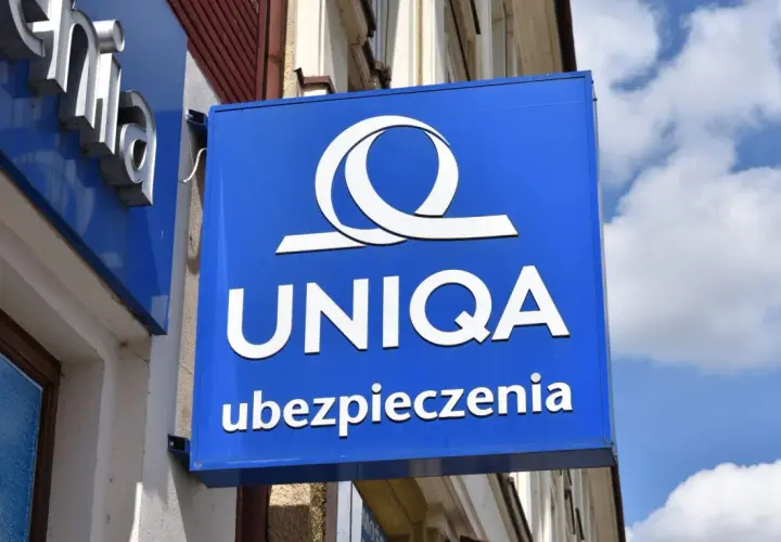 Niebieski szyld z logo i napisem "UNIQA ubezpieczenia". Firma UNIQA oferuje ubezpieczenia.
