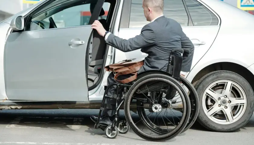 Mężczyzna na wózku inwalidzkim wsiada do samochodu. Ubezpieczenie samochodu a stopień niepełnosprawności to ważna kwestia dla osób z niepełnosprawnościami.