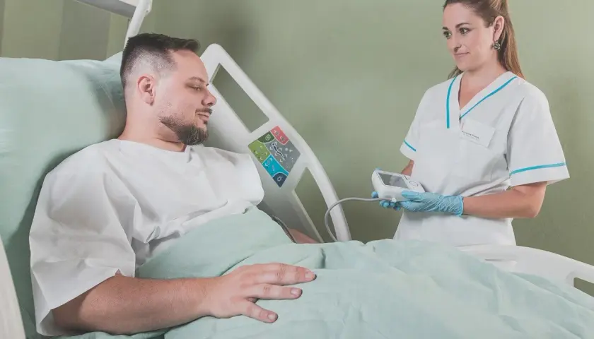 Uśmiechnięta pielęgniarka z aparatem do pomiaru ciśnienia w rękach, pacjent w łóżku szpitalnym. Radość z zakończenia leczenia.