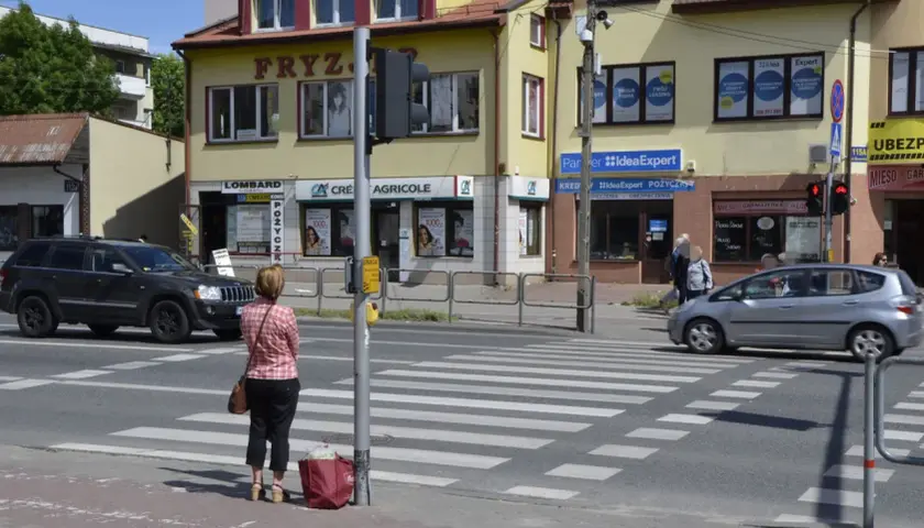Kobieta czeka na zielone światło na pasach, kiedy należy zachować szczególną ostrożność. Samochody zbliżają się do przejścia.