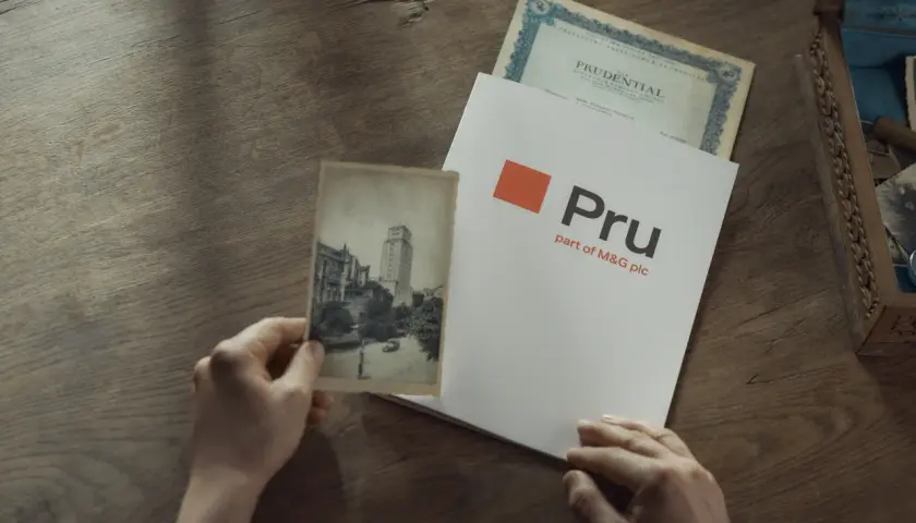 Ręce trzymają stare zdjęcie i dokument z logo Pru, part of M&G plc. To pokazuje, że Prudential to firma z długą historią.
