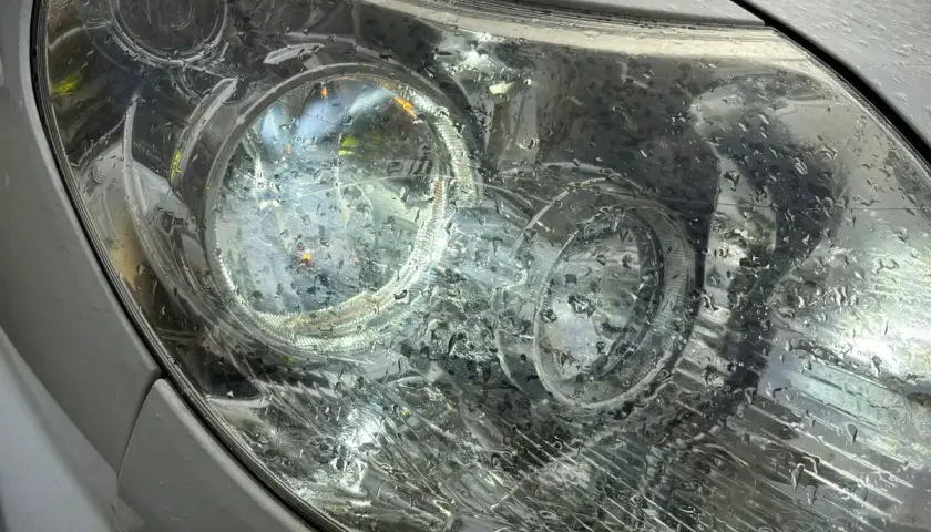 Krople deszczu na reflektorze, który świeci, sugerują jazda bez jednego światła.