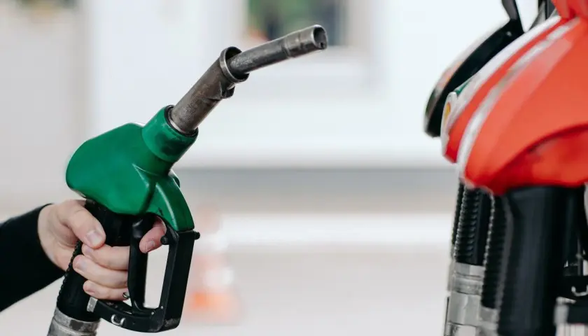 Dłoń trzyma zielony pistolet dystrybutora paliwa. Czy to benzyna 95 czy 98? Różnica jest ważna dla silnika.