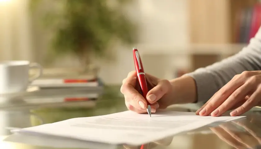 Dłoń pisze czerwonym długopisem na dokumencie. Zastanawiam się, co dalej, gdy nie wypowiedziałem umowy OC.
