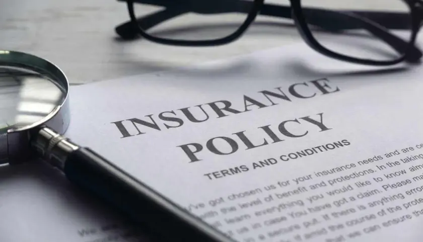 Okulary, lupa i dokument "Insurance Policy" symbolizują analizę polisy PZU po śmierci teścia.