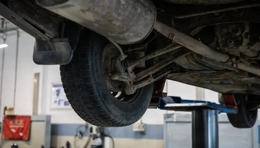 Podnośnik samochodowy ukazuje podwozie auta, gdzie widać koło i elementy zawieszenia. Może to być etap przygotowań do zwrotu autocasco po sprzedaży samochodu.