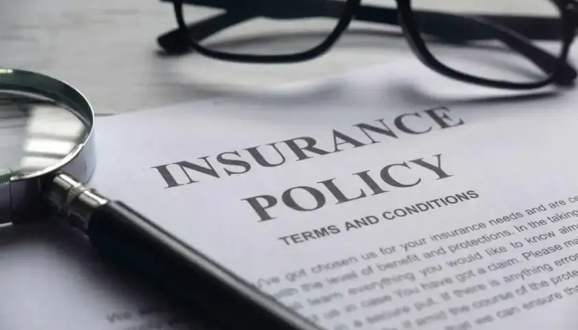 Okulary i lupa nad dokumentem "Insurance Policy". Zastanawiasz się, odszkodowanie za śmierć teścia ile?
