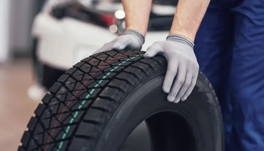 Mechanik w rękawiczkach trzyma oponę zimową. Czy w Polsce jest obowiązek zmiany opon na zimowe? Odpowiedź brzmi: nie.