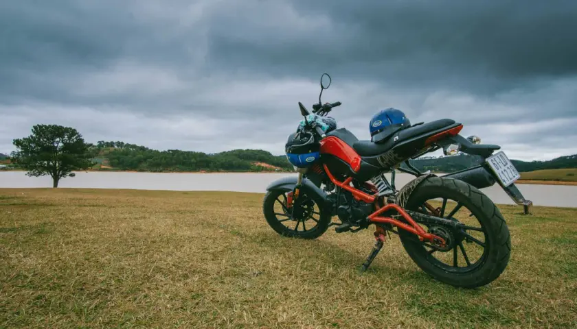 Czerwono-czarny motocykl z niebieskim kaskiem na siedzeniu, gotowy do jazdy nad jeziorem.